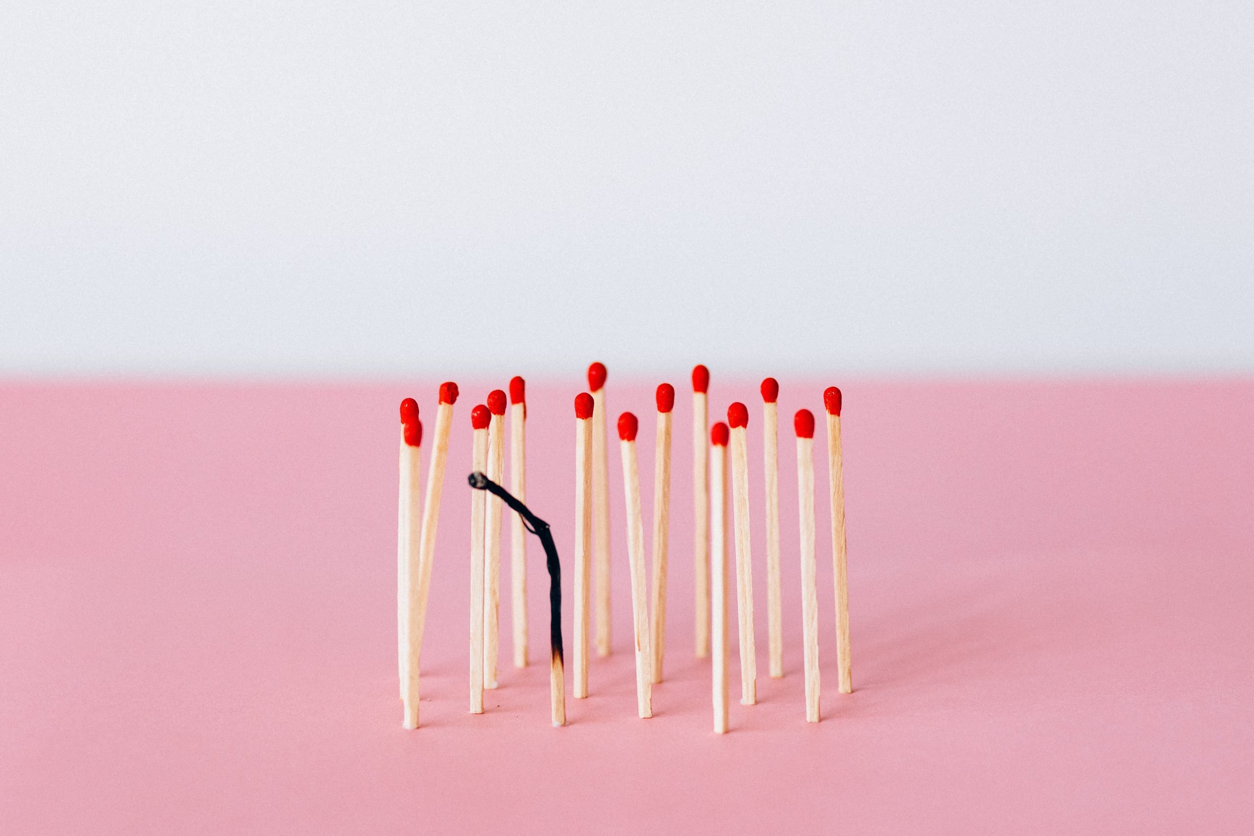 A pink background with matchsticks standing upright and one matchstick in the front is burnt black.