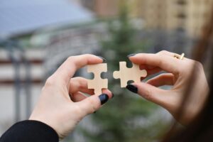 A pair of hands with black painted fingernails, each hand holding a puzzle piece that fits the other.