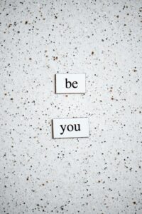 A sprinkled pattern white background and two words written in black, Be You.