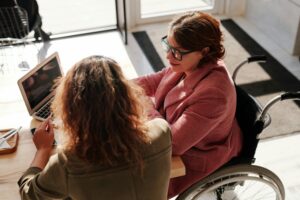 Two women sit side by side at a coffee shop as the sunlight shines on the table giving a warm feeling.